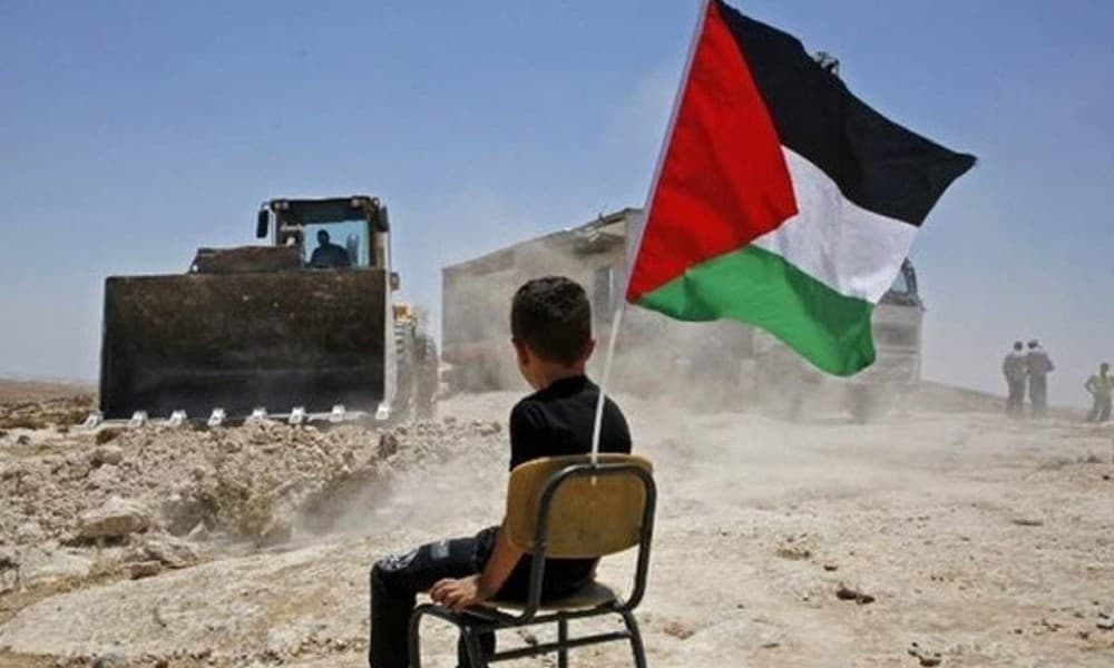 Seorang anak Palestina di bawah bendera negaranya sedang memandang kendaraan alat berat Israel